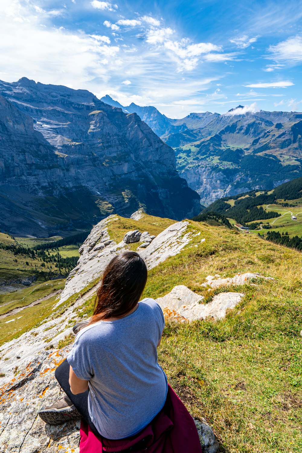 a woman sitting on a rock looking at the mountains