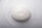 A smooth, oval-shaped white soap bar embossed with a simple bird design rests on a glossy white surface.