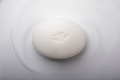 A smooth, oval-shaped white soap bar embossed with a simple bird design rests on a glossy white surface.