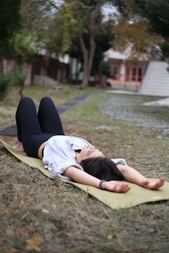 a woman laying on a yoga mat in a park