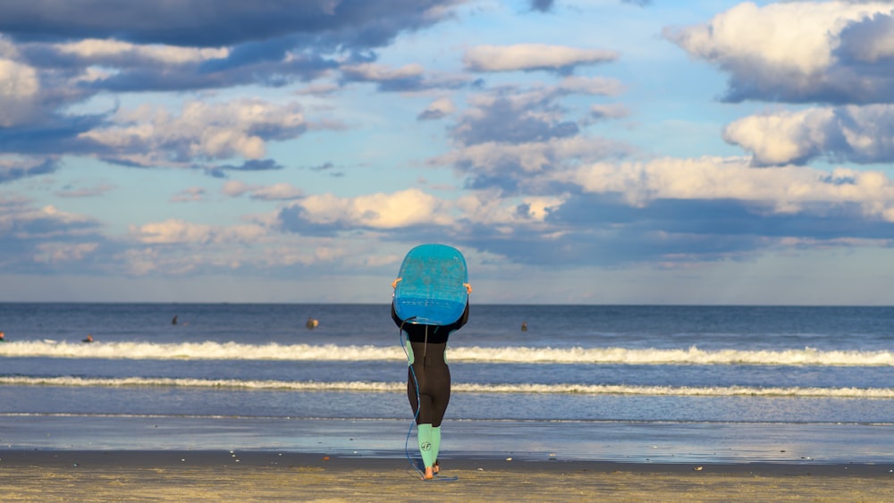 a person standing on a beach with a surfboard on their head