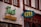 The image displays a building facade with two distinct signs. One sign features the text 'Frosch' in green neon script above 'PARFUMERIE' in yellow block letters. Another sign has '4711' in yellow against a teal background. The facade is primarily white with brown accents, and there are windows with red-brown trim visible above the signs.