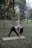 A man doing yoga on a mat in a sunny park with trees around.