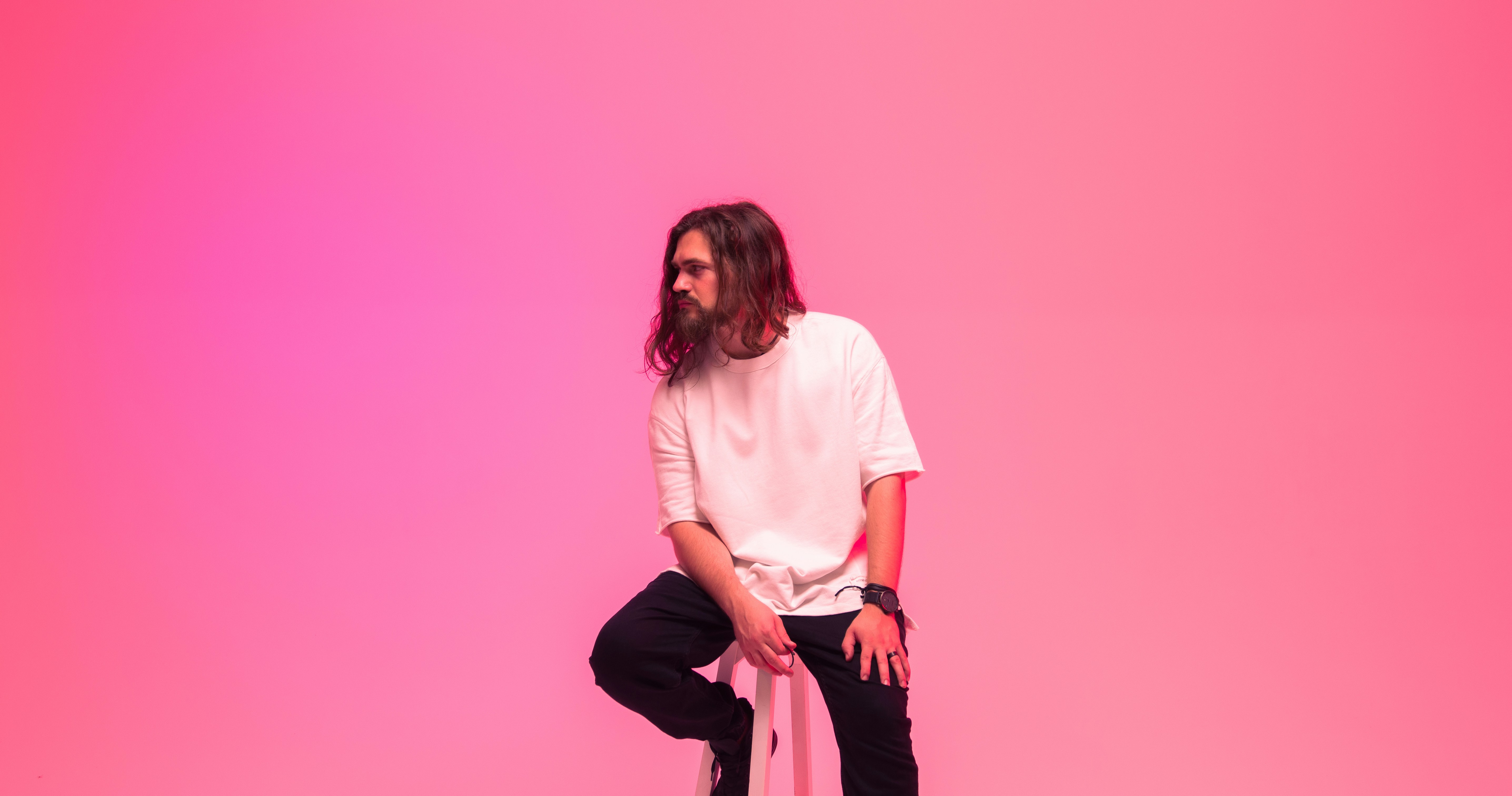 a man with long hair sitting on a stool