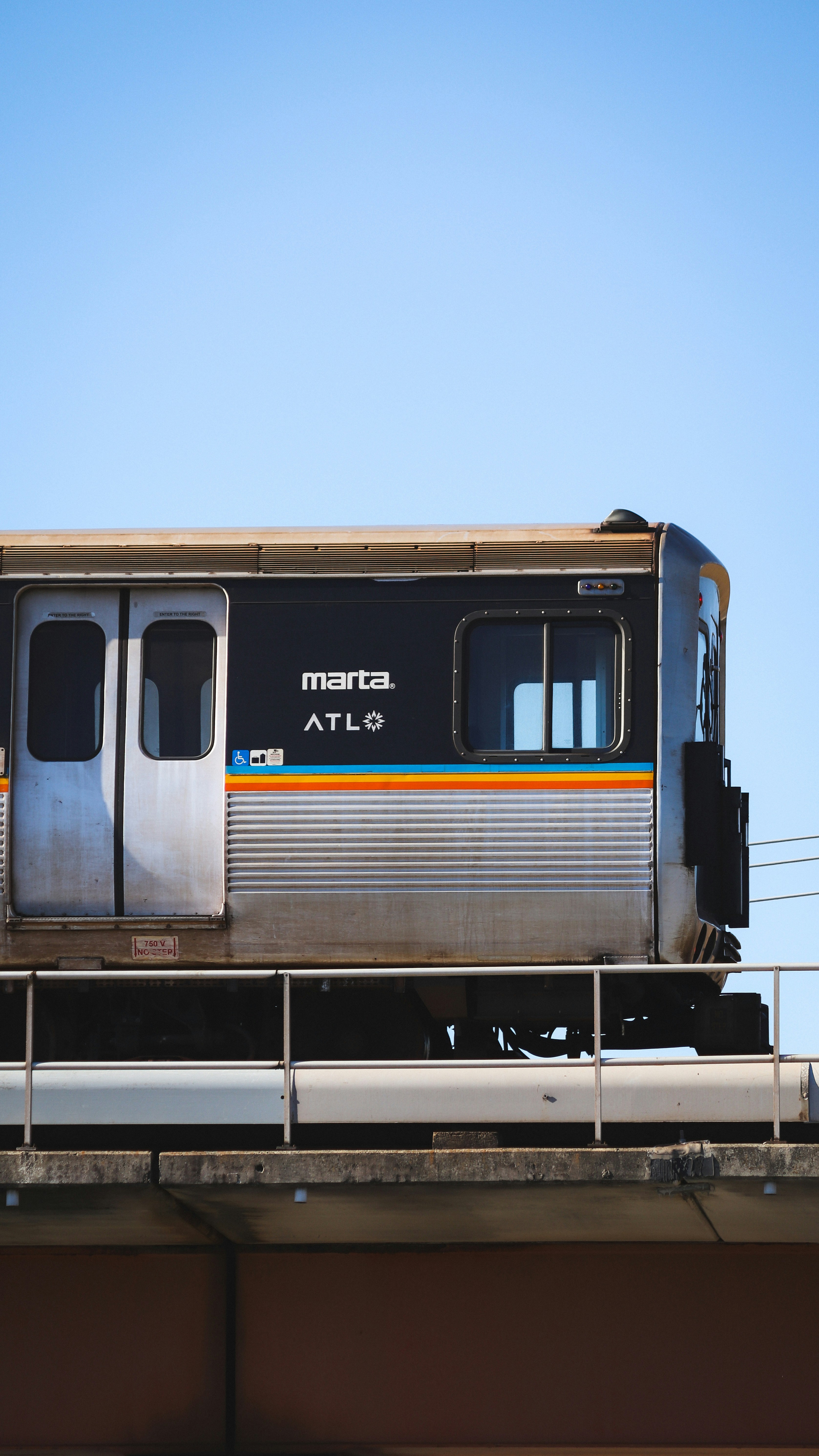 a silver train traveling over a bridge under a blue sky