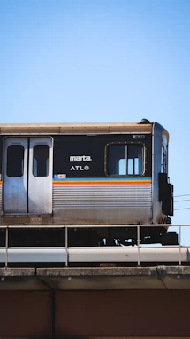 a silver train traveling over a bridge under a blue sky