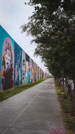 Community artists painting a mural with traditional Mexican motifs and vibrant colors along a canal pathway.