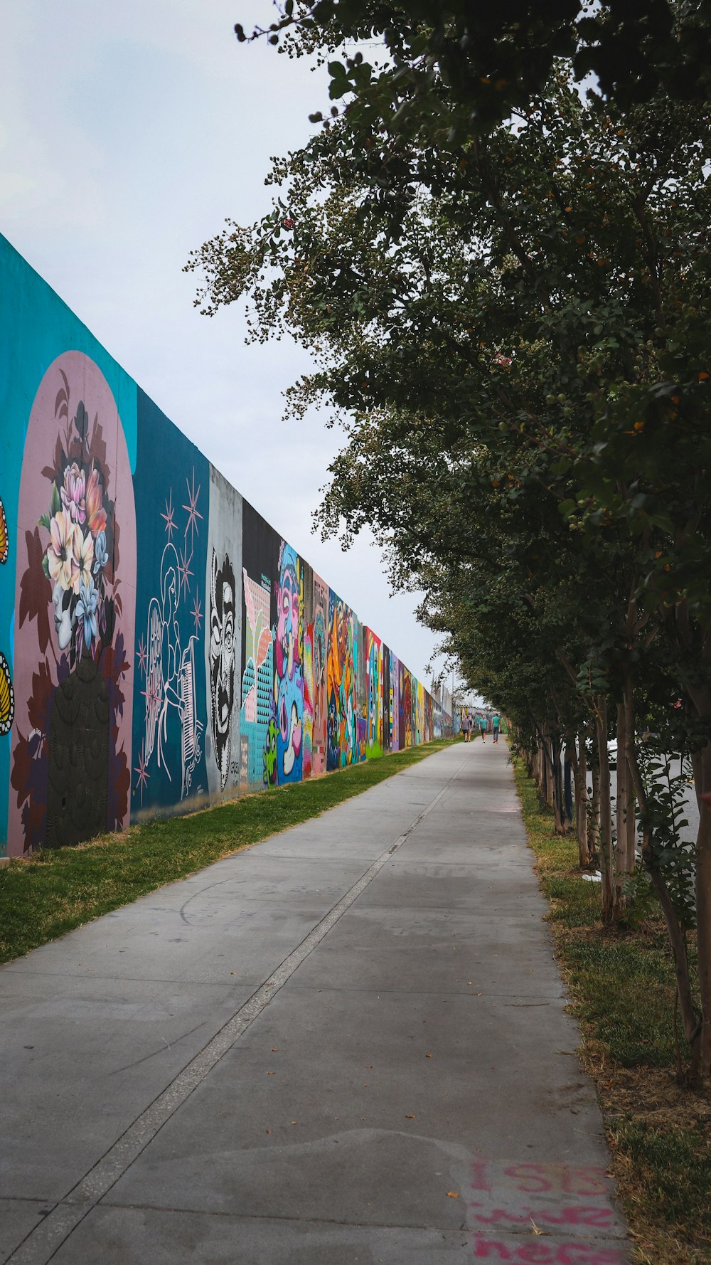 a sidewalk with a row of trees next to a colorful wall