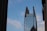 A tall, modern skyscraper with a unique split design at the top, featuring glass windows and structural supports. There is a large logo displayed near the top with the text 'King & Spalding'. The sky is blue with scattered clouds, and there is a thin wire crossing the image diagonally with birds perched on it. Nearby buildings partially frame the scene on both sides.