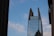 A tall, modern skyscraper with a unique split design at the top, featuring glass windows and structural supports. There is a large logo displayed near the top with the text 'King & Spalding'. The sky is blue with scattered clouds, and there is a thin wire crossing the image diagonally with birds perched on it. Nearby buildings partially frame the scene on both sides.