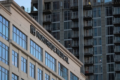 A modern building with the sign 'Northside Medical' prominently displayed. The structure features large glass windows reflecting the light. In the background, there is a high-rise apartment building with numerous balconies and windows, showcasing an urban setting.