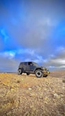 A rugged SUV standing on a dirt trail beneath a vibrant blue sky.