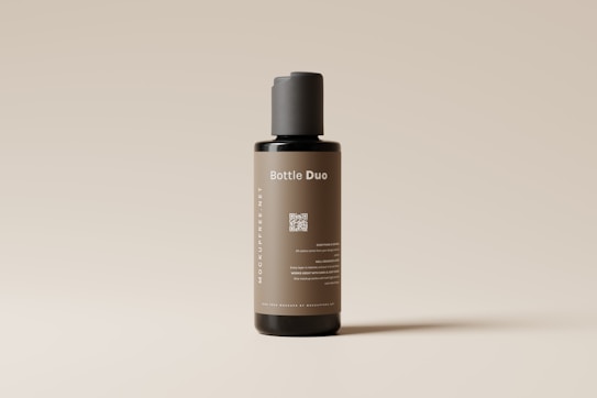 A sleek, cylindrical bottle with a minimalist design stands against a light neutral background. The label on the bottle reads 'Bottle Duo' in white text, and there is a QR code printed below it. The bottle's color is a muted brown with a black cap, and additional text is displayed vertically along the side.