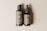 Two bottles are placed side by side on a neutral beige background. The larger bottle has a pump dispenser, while the smaller bottle features a dropper. Labels on both bottles read 'Bottle Duo' with detailed text below, including a QR code. The bottles have a sleek and minimalist design.