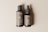 Two bottles are placed side by side on a neutral beige background. The larger bottle has a pump dispenser, while the smaller bottle features a dropper. Labels on both bottles read 'Bottle Duo' with detailed text below, including a QR code. The bottles have a sleek and minimalist design.