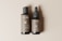 Two bottles are placed side by side on a neutral beige background. The larger bottle has a pump dispenser, while the smaller bottle features a dropper. Labels on both bottles read 'Bottle Duo' with detailed text below, including a QR code. The bottles have a sleek and minimalist design.