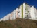 Several modern apartment buildings with multiple floors and colorful facades, including green, white, and orange panels. The buildings are situated on a sloped grassy area under a clear blue sky.