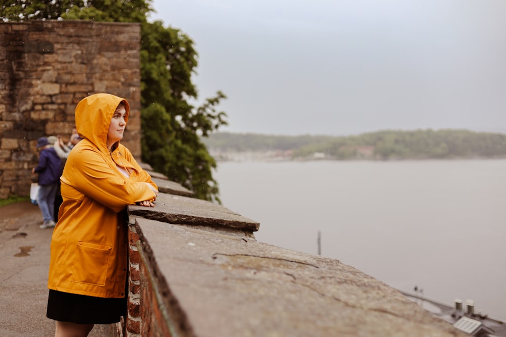 a woman in a yellow jacket leaning on a brick wall