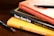 A stack of books is arranged on a wooden surface. The books include 'Aristotle's Nicomachean Ethics', 'Think & Grow Rich' by Napoleon Hill, and 'The Energy Bus'. Additionally, there are two fountain pens placed around the stack.