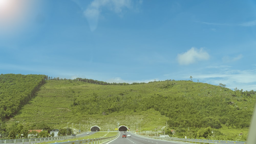 a car driving down a road next to a lush green hillside