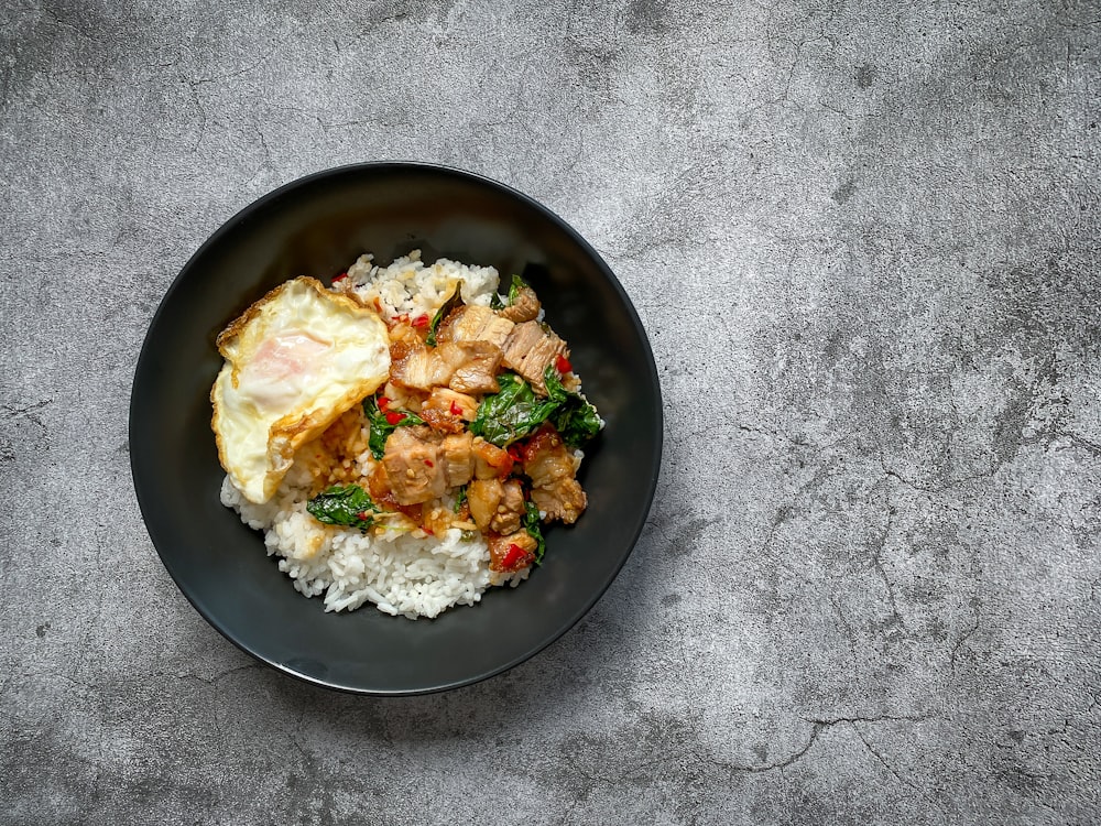 a black plate topped with rice and meat