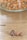 Three coffee beans are placed on a wooden surface with a blurred background showing a glass container filled with various nuts.