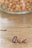 Three coffee beans are placed on a wooden surface with a blurred background showing a glass container filled with various nuts.