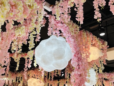 A ceiling decorated with cascading pink and cream artificial flowers. Large, cloud-like pendant lights hang among the floral arrangements, casting a soft glow. The black ceiling contrasts with the colorful, delicate blooms.