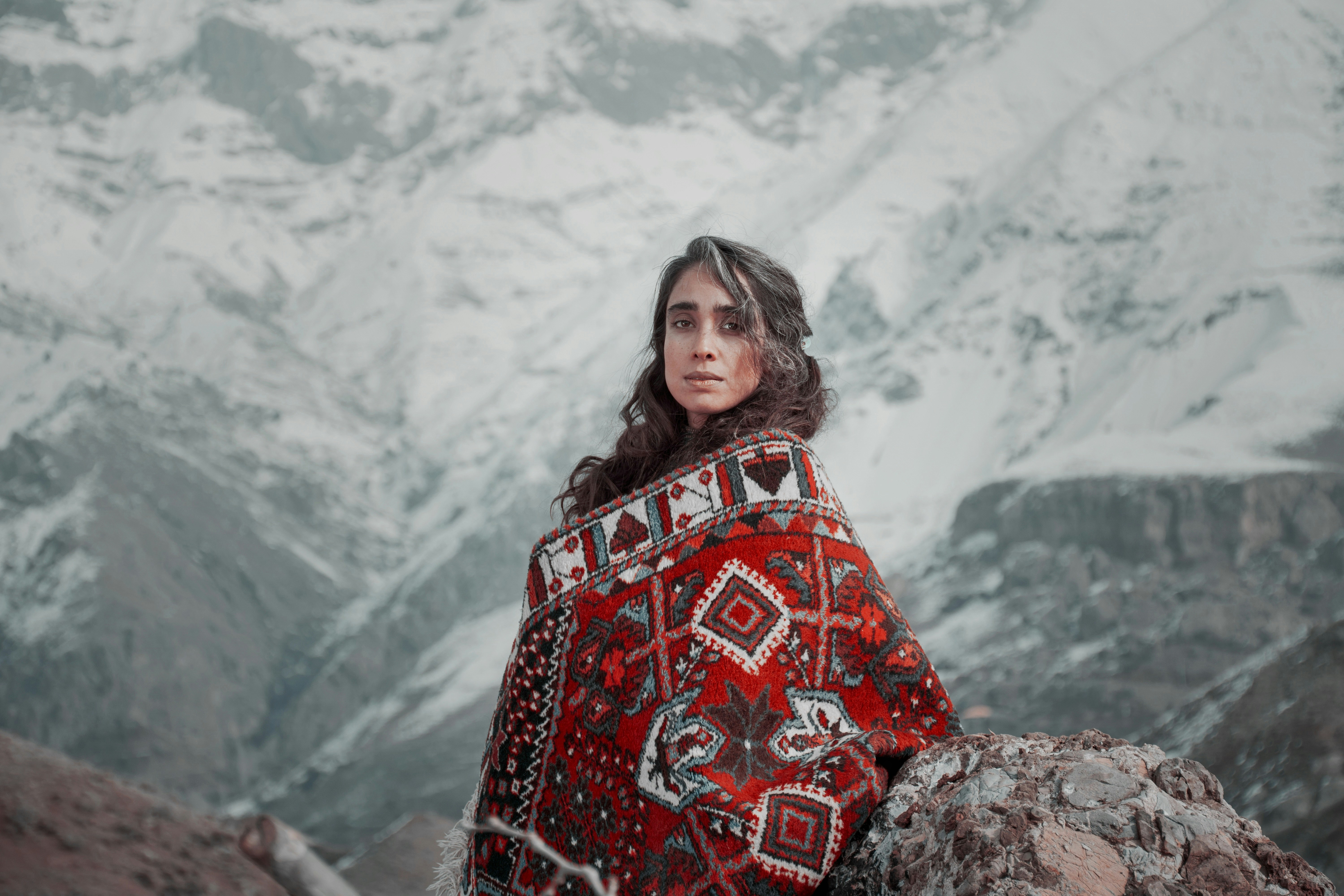 a woman in a red and black blanket sitting on a rock