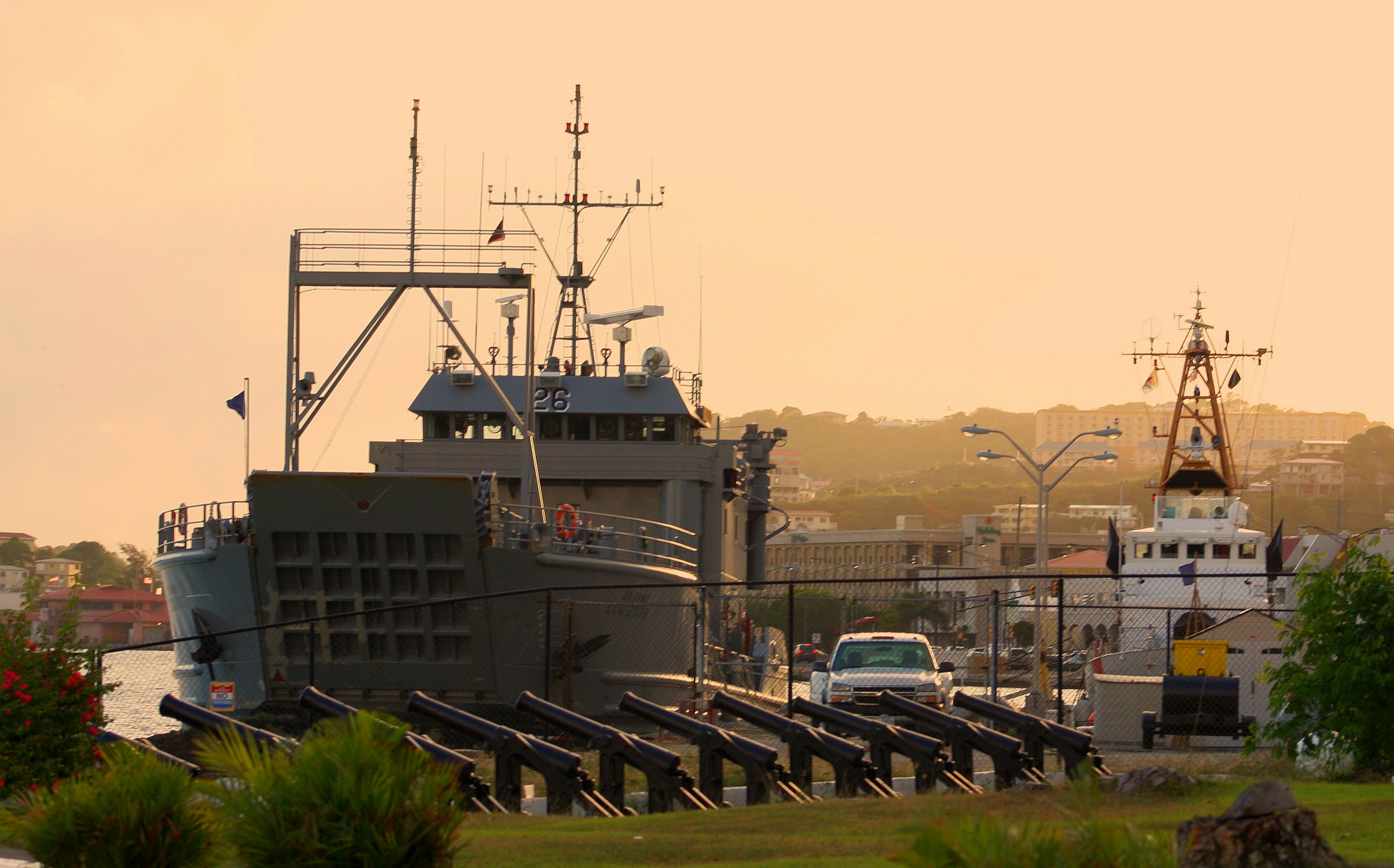 a large boat is docked in a harbor, A military transport ship docks near a row of historic cannons.