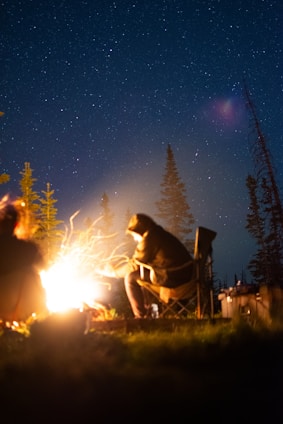 A rugged survivalist reading a weathered manual beside a campfire under a starry night.
