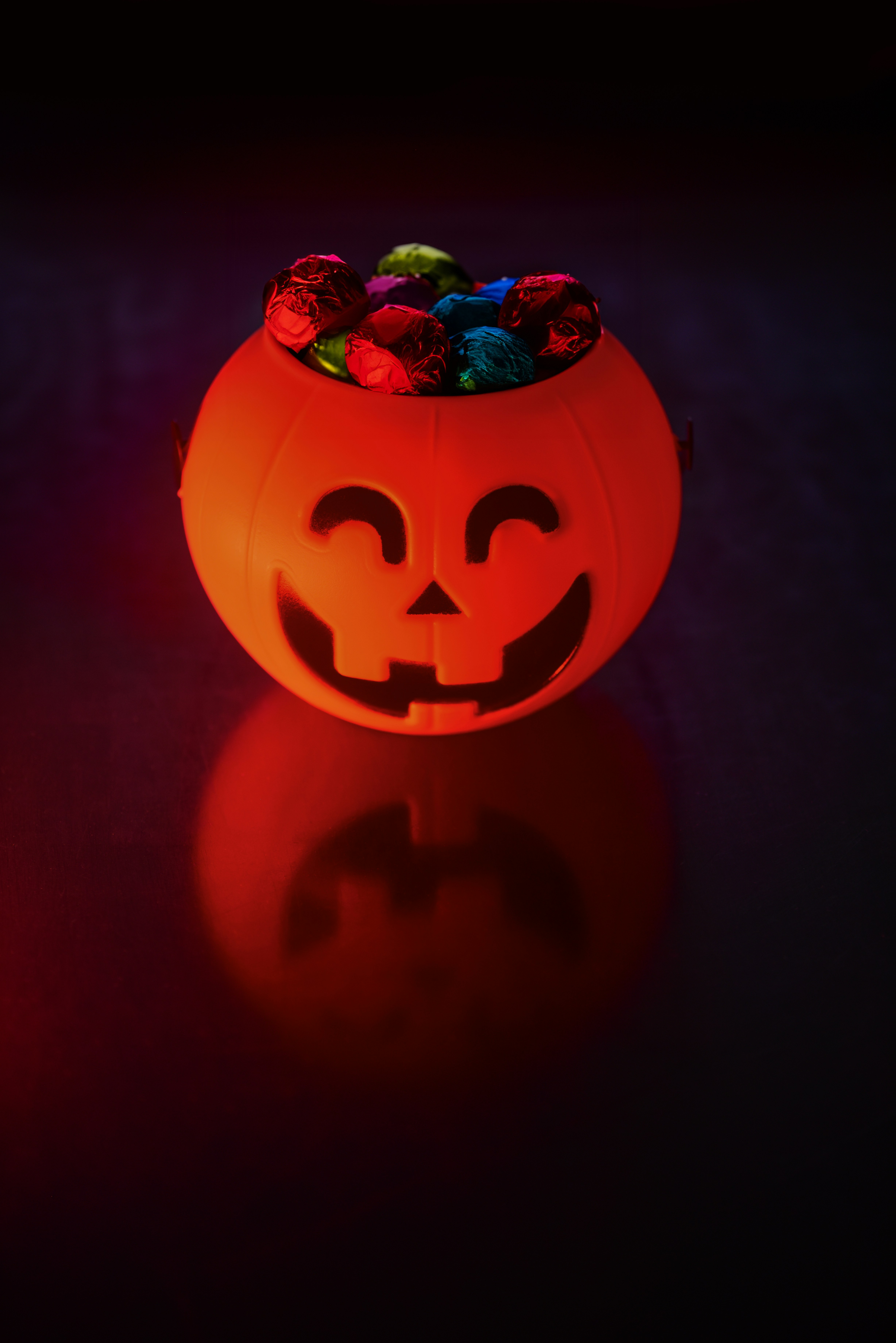 Orange pumpkin bucket overflowing with assorted Halloween candy and chocolate bars