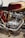 A close-up view of a detailed classic motorcycle engine, featuring polished metal and chrome components. The red and gold color scheme on the bodywork complements the intricate design of the mechanical parts.