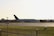 A large airplane with Qatar Airways branding is positioned on an airport runway during daylight. The aircraft is seen from a side view, and there is a control tower visible on the left side of the image. The area surrounding the runway is grassy, and the scene conveys a calm atmosphere.