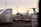 An aircraft is parked on an airport tarmac surrounded by storage containers labeled with logistics company brands. The scene is illuminated by a soft, warm light from the setting or rising sun, and several airport light poles are visible in the background.