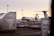 An aircraft is parked on an airport tarmac surrounded by storage containers labeled with logistics company brands. The scene is illuminated by a soft, warm light from the setting or rising sun, and several airport light poles are visible in the background.
