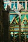 An intricate Art Deco architectural facade featuring geometric patterns and stylized motifs. The building uses a combination of green and gold reflective glass, framed by ornate metalwork. The design includes symmetrical fan-like decorations and angular shapes, creating a visually striking and harmonious appearance.