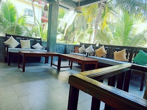 Outdoor seating area surrounded by flowering bushes and palm trees.