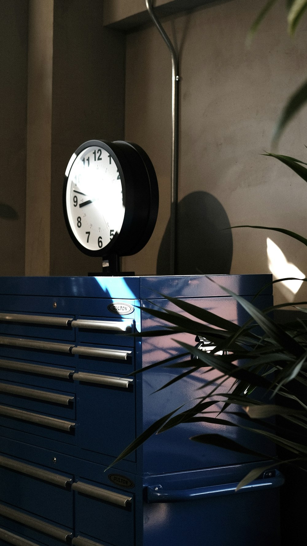 um relógio sentado em cima de um armário azul ao lado de uma planta