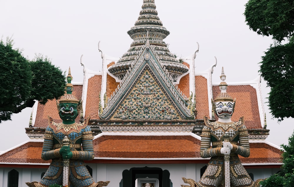 two statues in front of a building with a roof