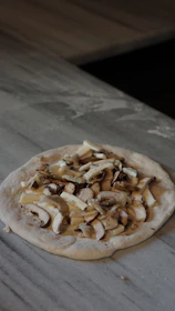 Chef carefully preparing pizza dough with fresh ingredients on a marble countertop.