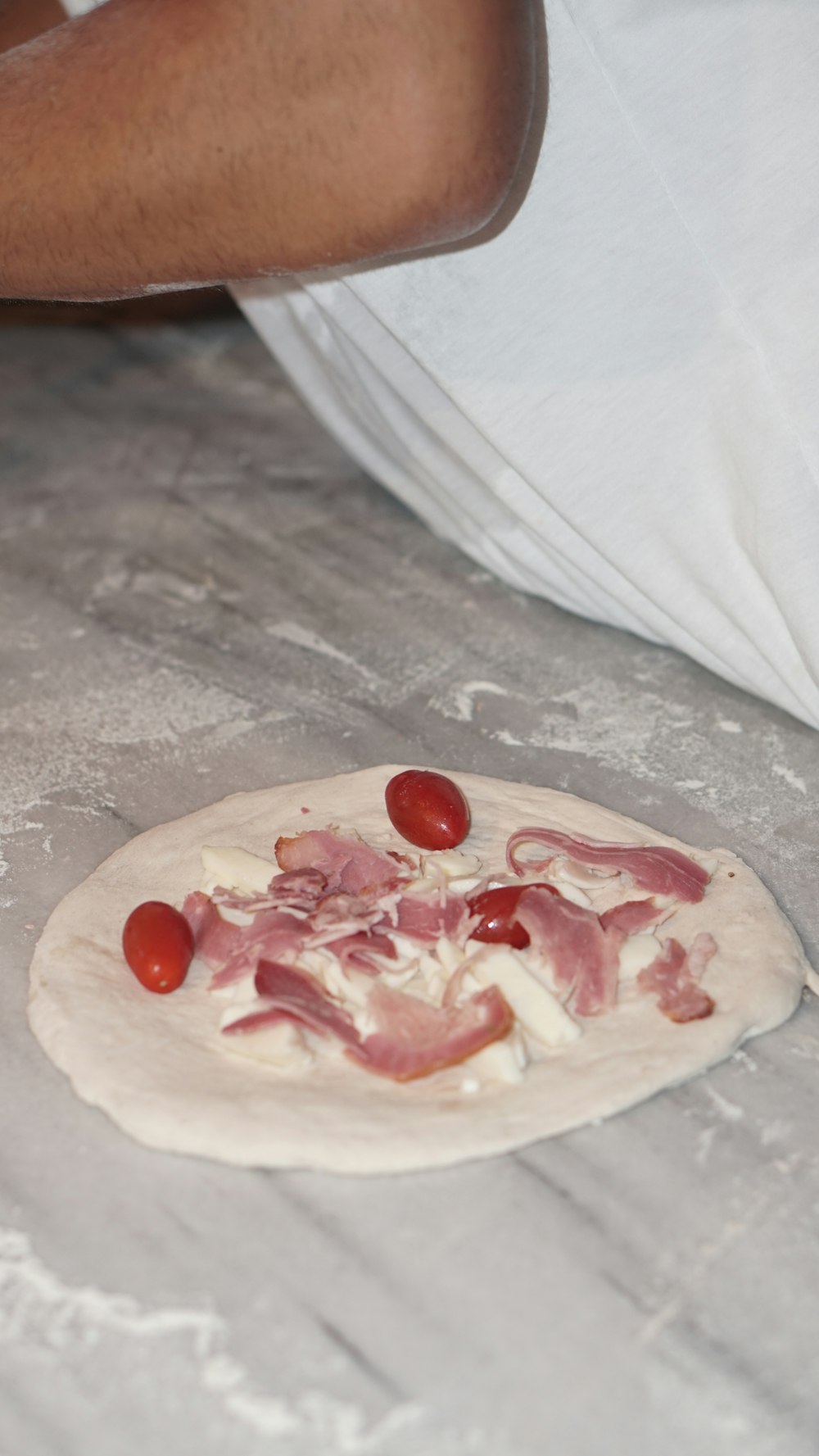 eine Person, die eine Pizza mit Schinken und Tomaten zubereitet