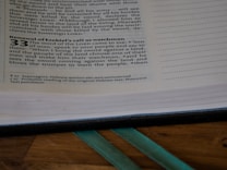 A close-up of a Bible page featuring text from the book of Ezekiel, chapter 33. The page is open on a wooden surface, and part of a ribbon bookmark is visible at the bottom. The text is printed in black on a white background, with certain headings and numbers bolded for emphasis.