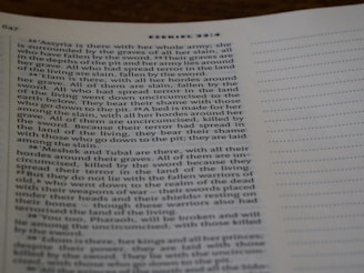 A close-up view of a page from a book, specifically a biblical text from Ezekiel 32:22-27. The page is slightly angled, and the text is printed on a white background with a visible margin on the right featuring perforated lines.