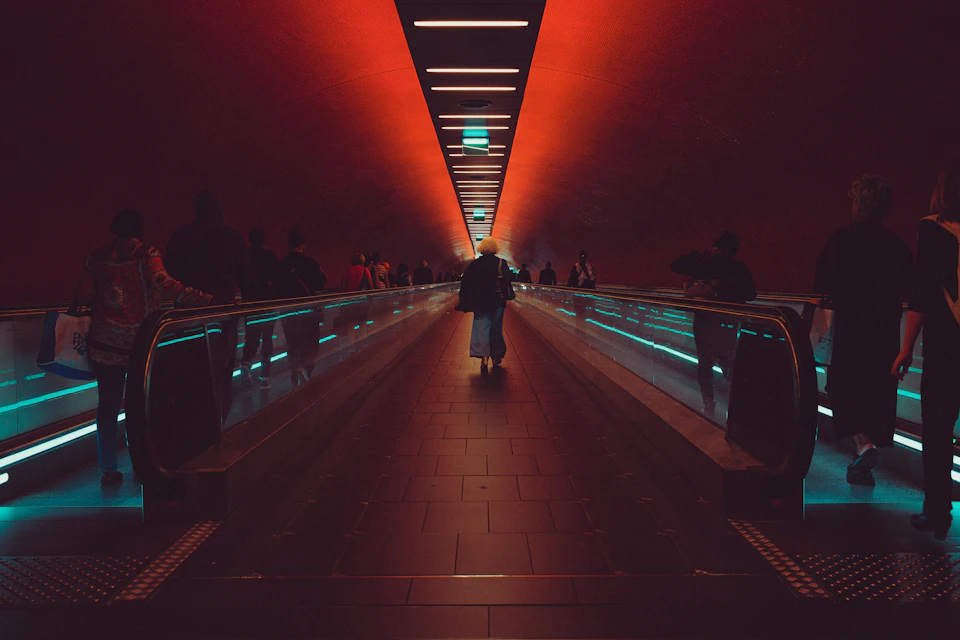 Long curved escalator with red wall and gray floor, filled with people walking upwards