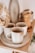 A set of rustic ceramic cups and plates are neatly arranged on a wooden shelf. The texture gives a handcrafted, artisanal feel. In the background, there are additional kitchen items, including a pepper grinder and a stack of bowls, adding to the cozy, homey atmosphere.