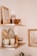 Two wooden shelves are mounted on a wall, displaying various home decor items. The top shelf holds a framed photo, a wine glass, a wooden bowl, and a tall candle. The lower shelf features stacked ceramic plates and bowls, a mug, a wooden pepper grinder, a sponge, and a soap bar.
