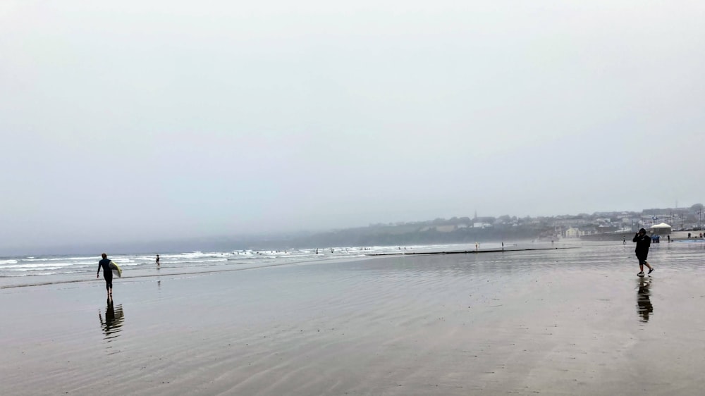 a couple of people walking along a wet beach