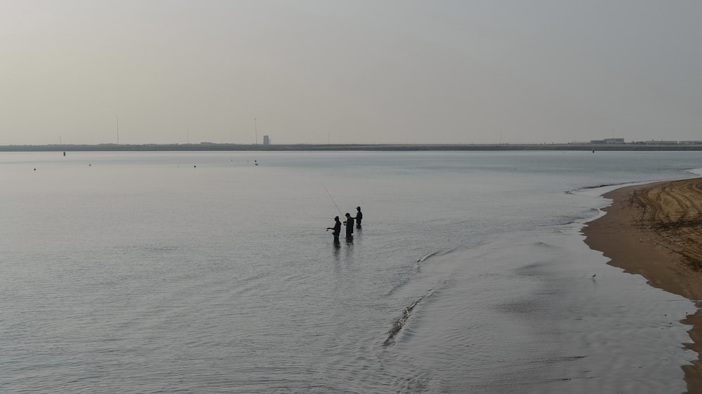 a couple of people standing on top of a beach next to a body of water