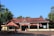 A traditional Indian temple with a terracotta-tiled roof and supporting columns, surrounded by lush greenery and palm trees. Several people are seen standing near the entrance, some wearing traditional attire.